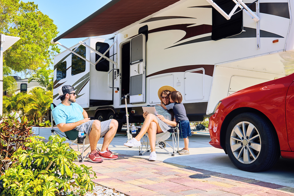 Family of 3 sitting outside of their RV at an RV park.