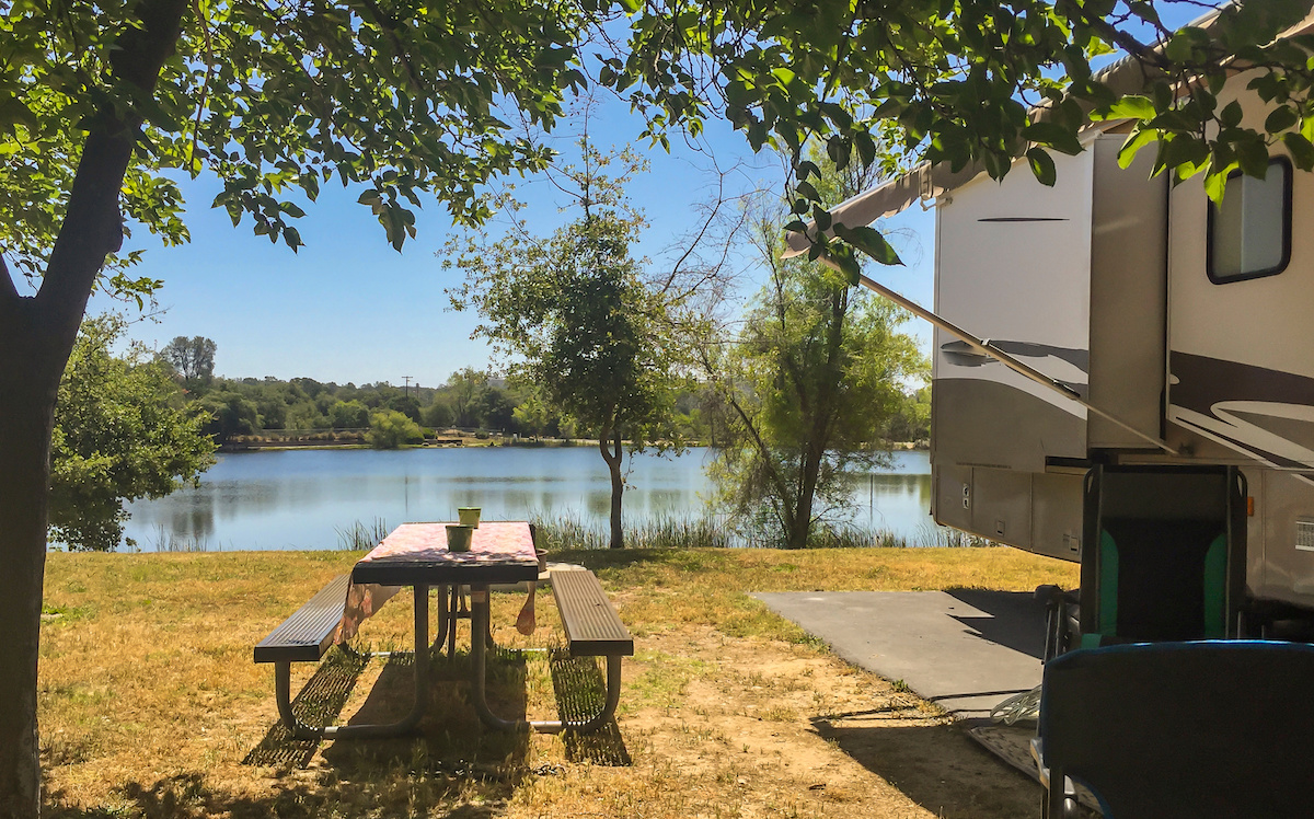 A picnic table next to an RV and lake on a campground. 