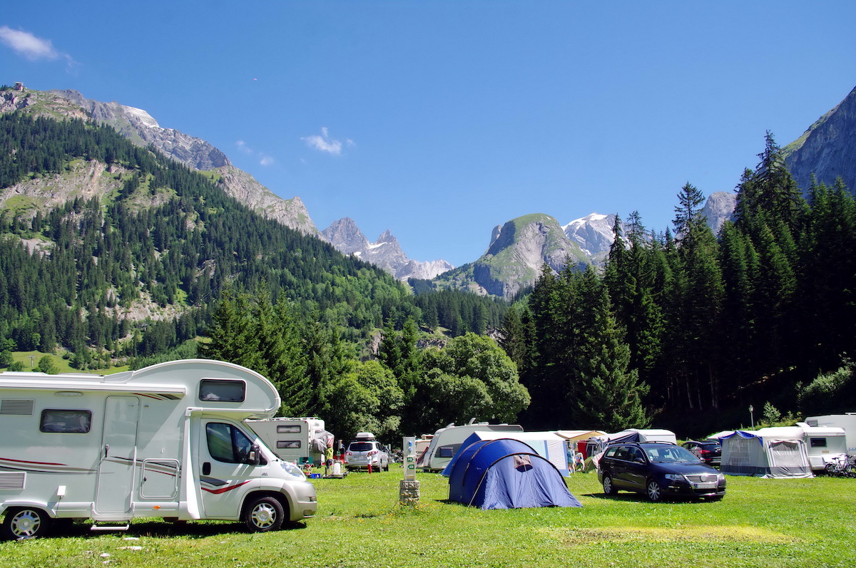 Campground with an RV and tents located next to a mountain. 