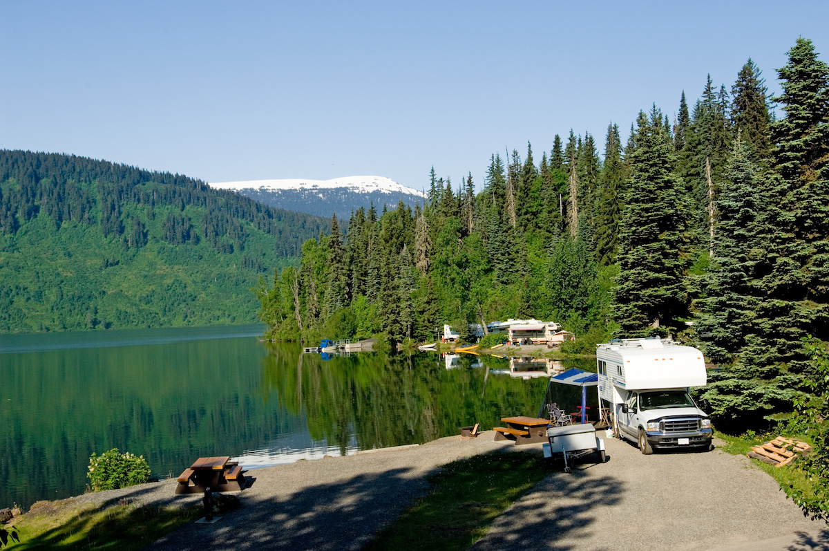 RV parked at a campground next to a forrest and lake. 